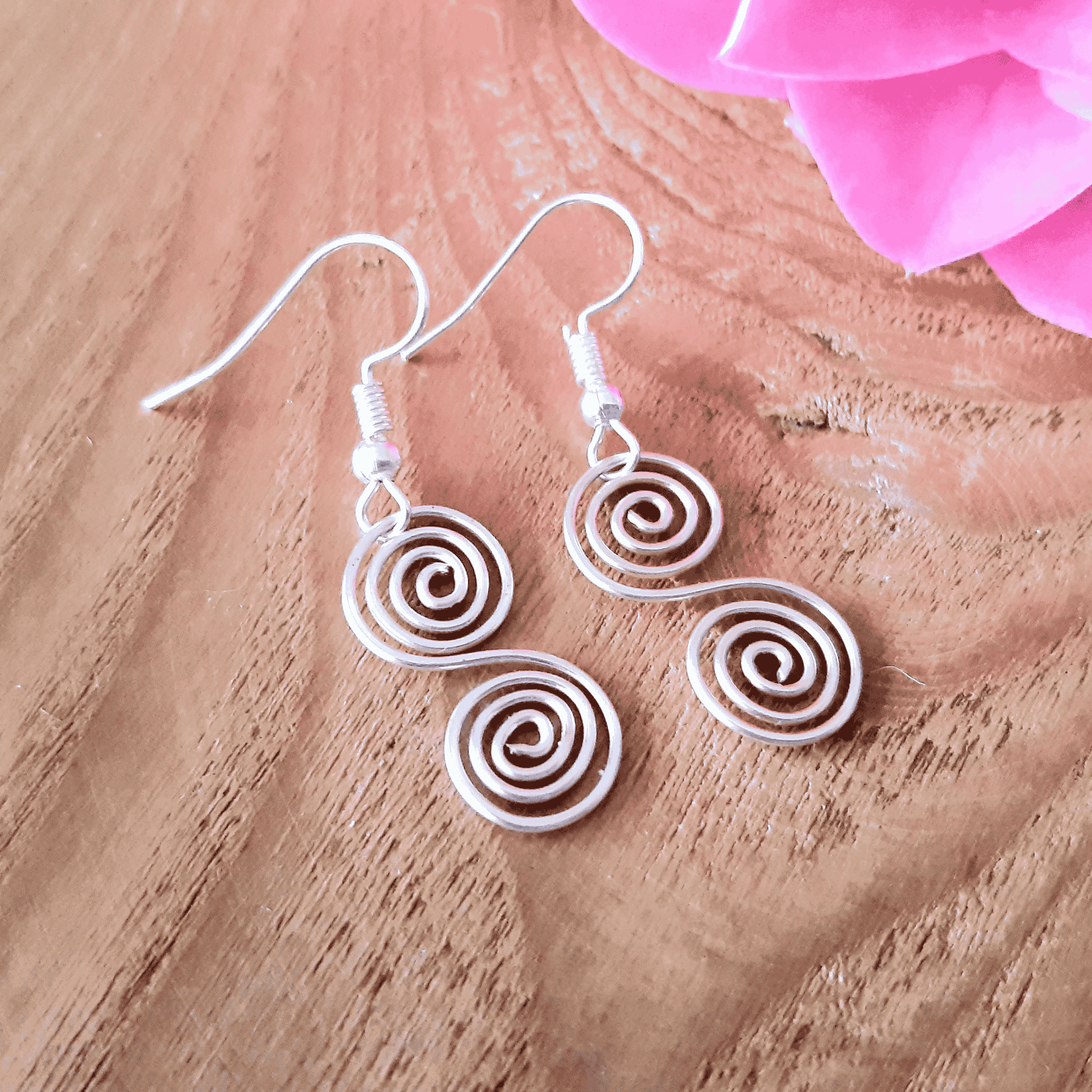Pair of spiral earrings on a wooden surface with a pink flower in the background
