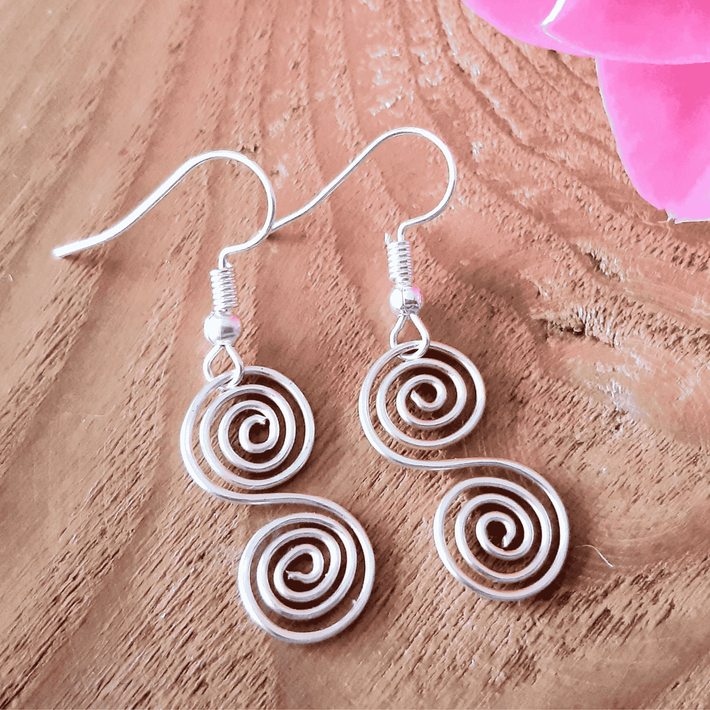 Silver spiral earrings on a wooden surface with pink flowers.