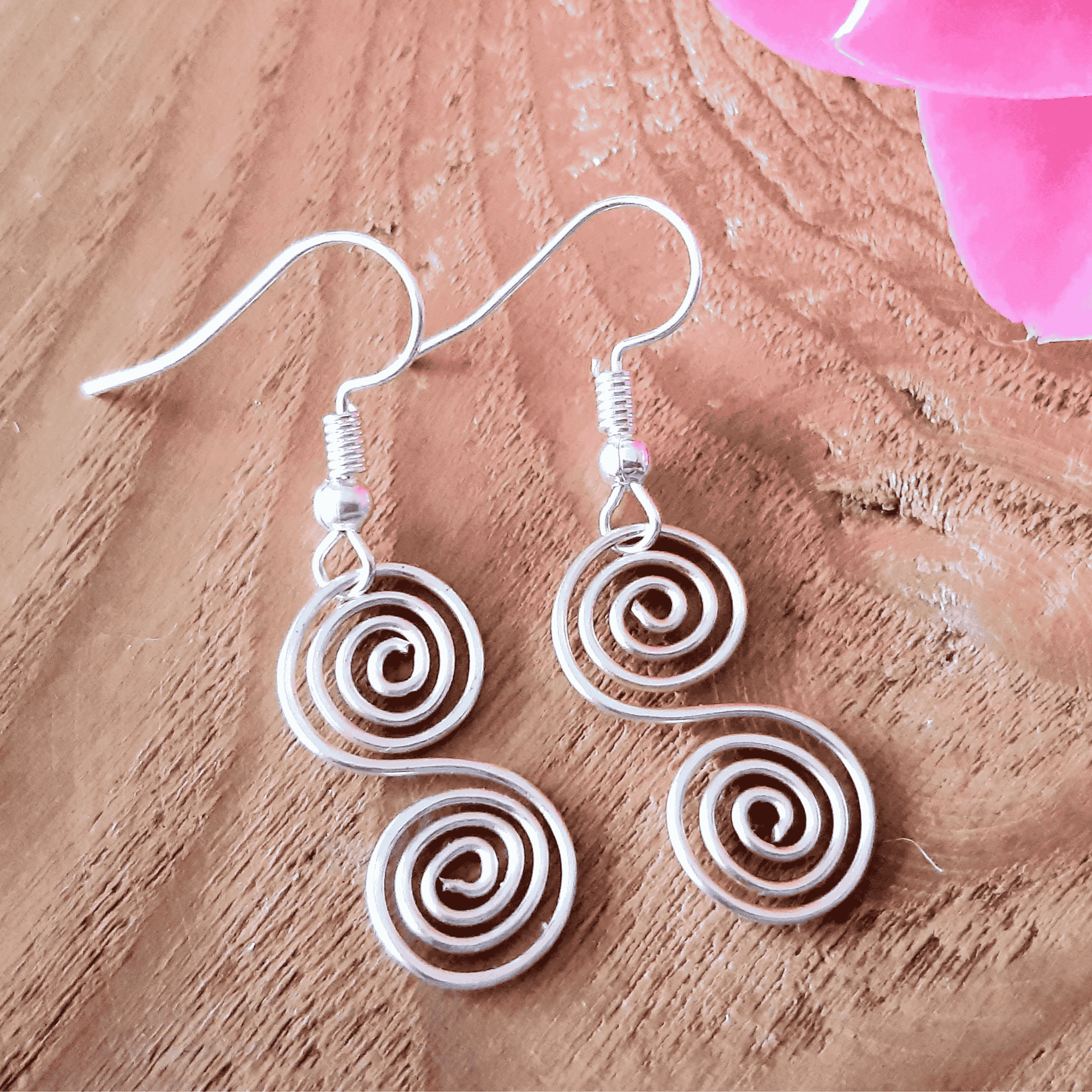 Silver spiral earrings on a wooden surface with pink flowers.