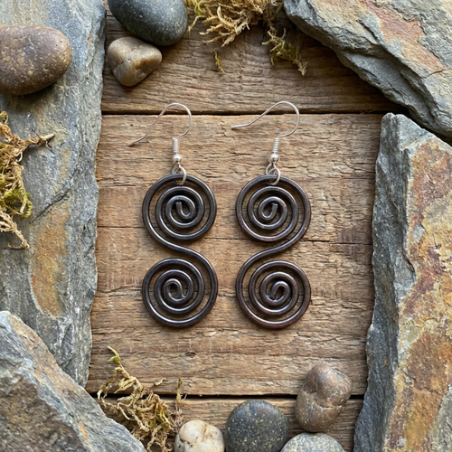 Dainty copper Celtic spiral earrings on a wooden and slate surface