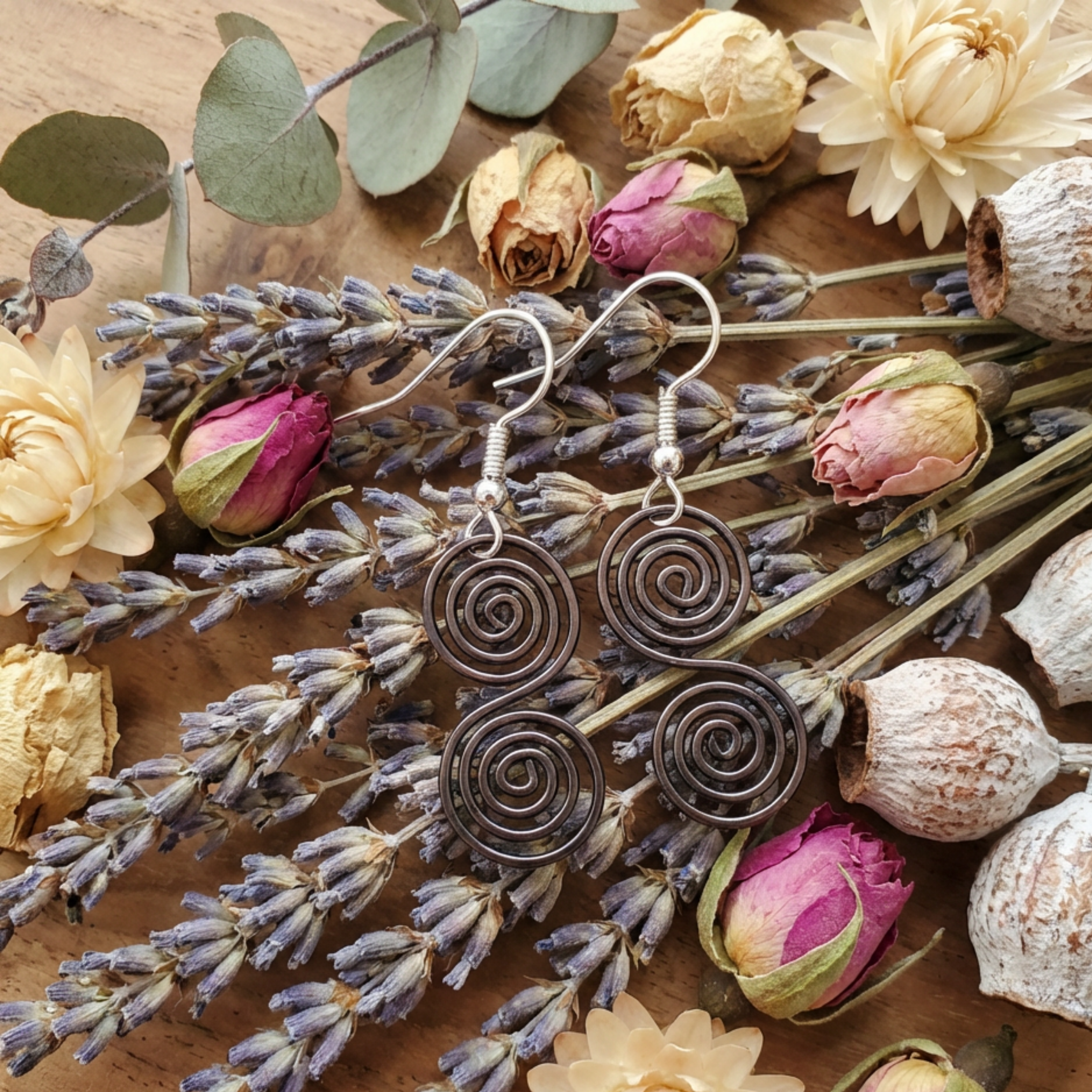 Celtic copper spiral earrings on light wood background, handmade copper jewellery UK