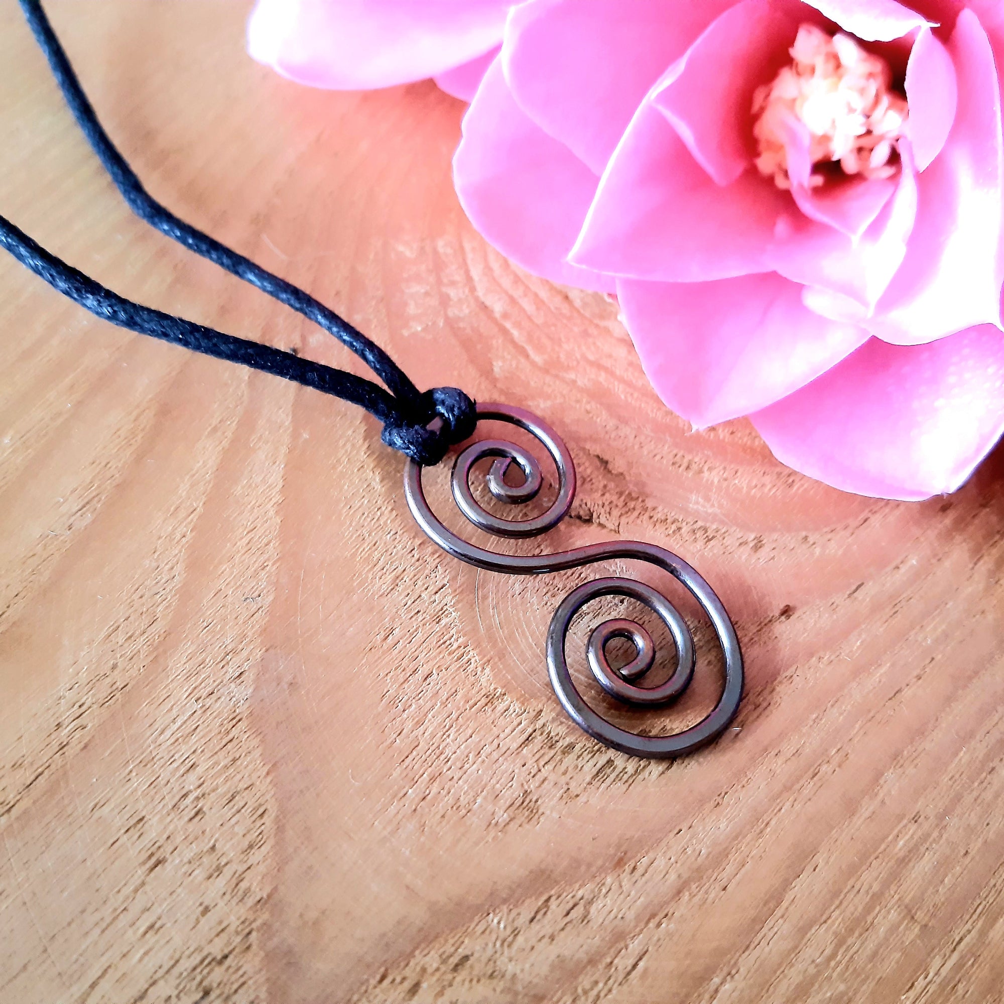 Necklace with spiral pendant on a wooden surface with pink flowers