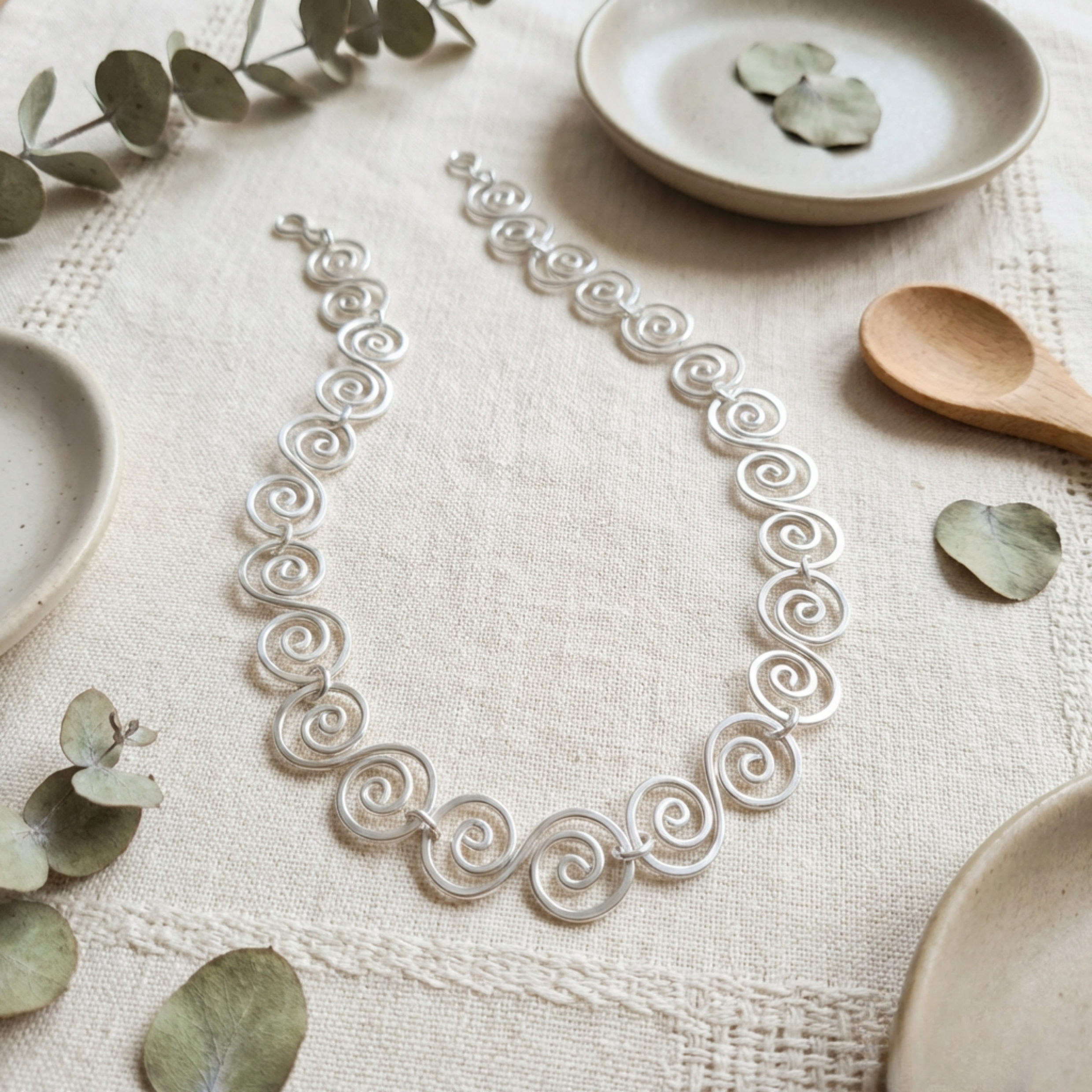 Celtic Silver necklace on a textured surface with ceramic plates and leaves