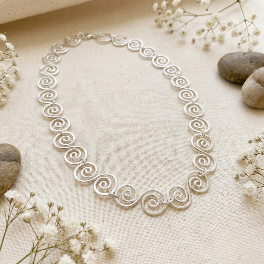 Silver necklace with intricate design on a beige fabric background with small flowers and stones.