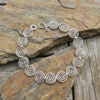 S shaped Celtic silver spiral bracelet on a stone surface
