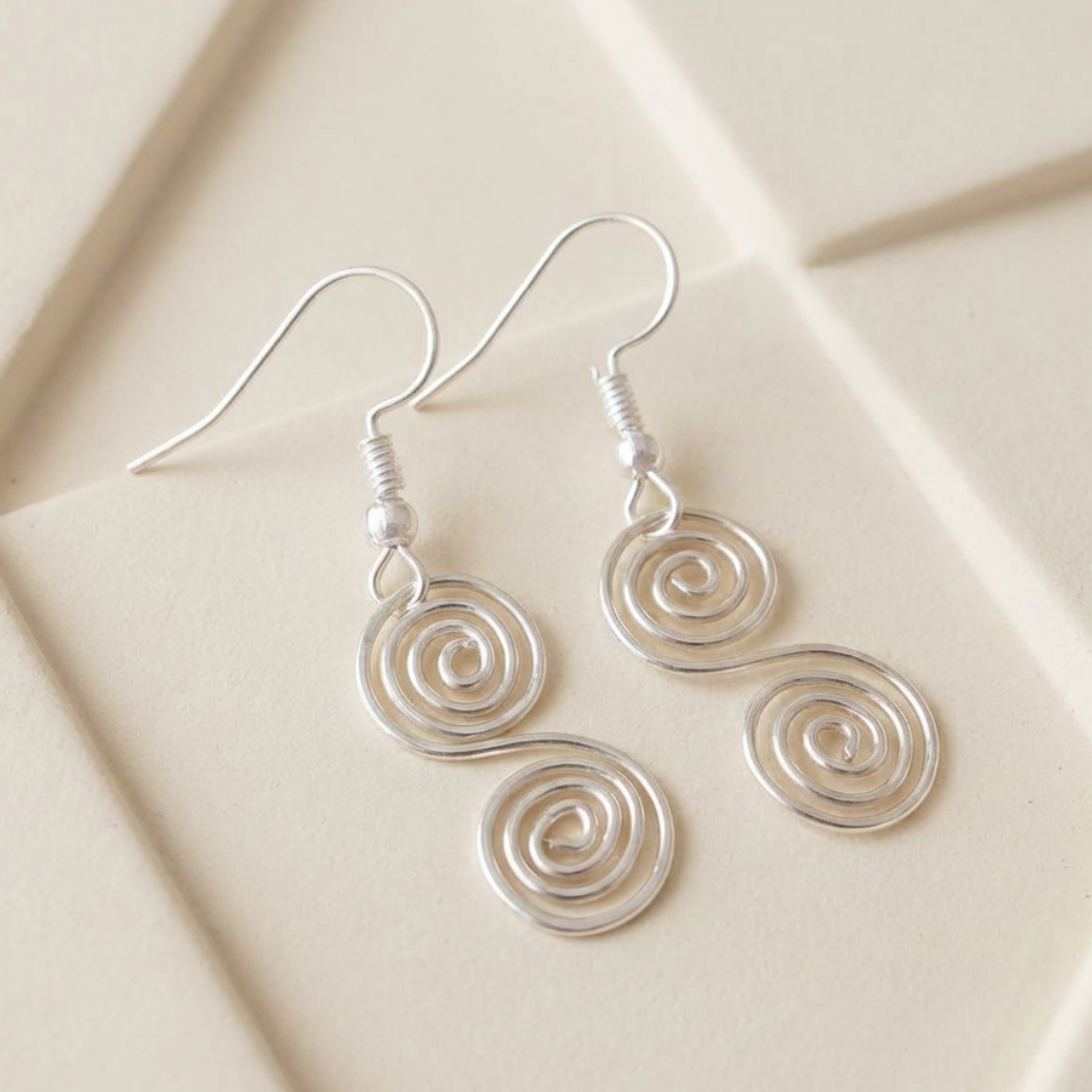 Silver spiral earrings on a beige surface