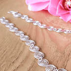 Decorative silver spiral necklace on a wooden surface with pink flowers in the background showing the detail of each spiral