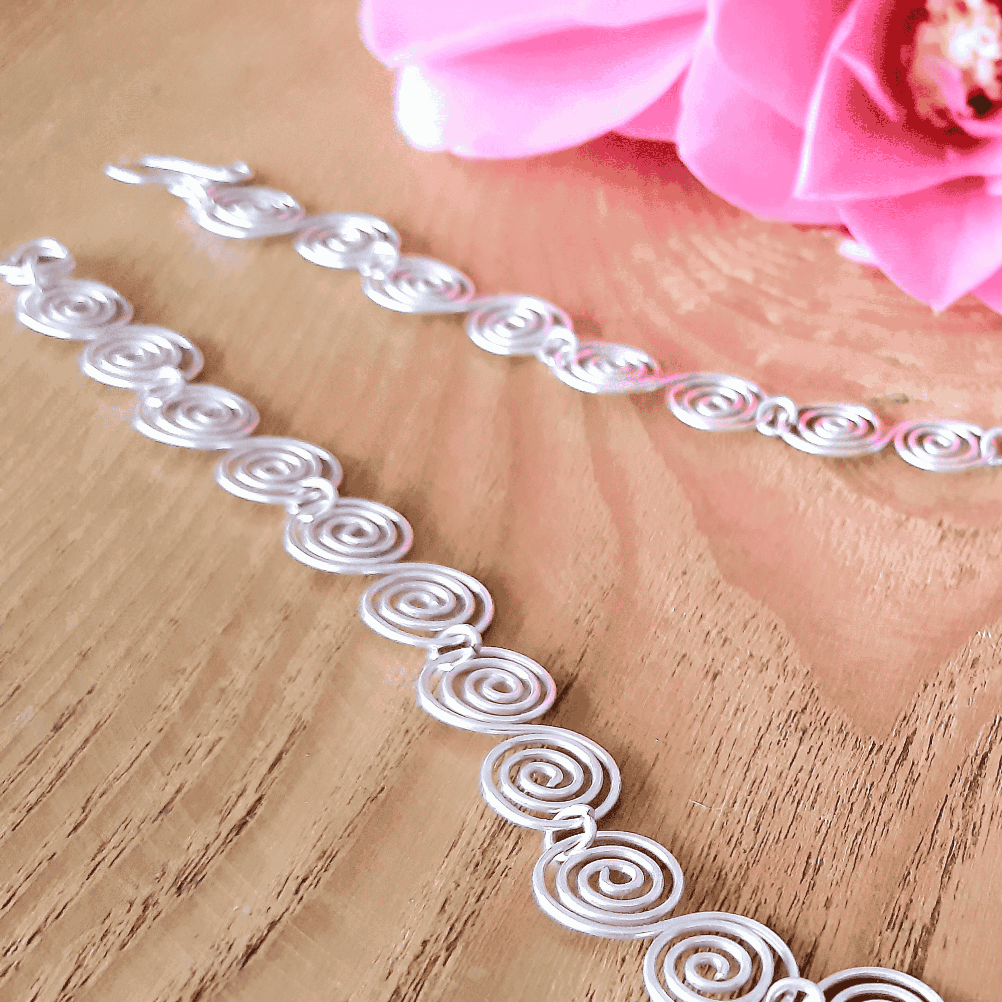 Decorative silver spiral necklace on a wooden surface with pink flowers in the background showing the detail of each spiral
