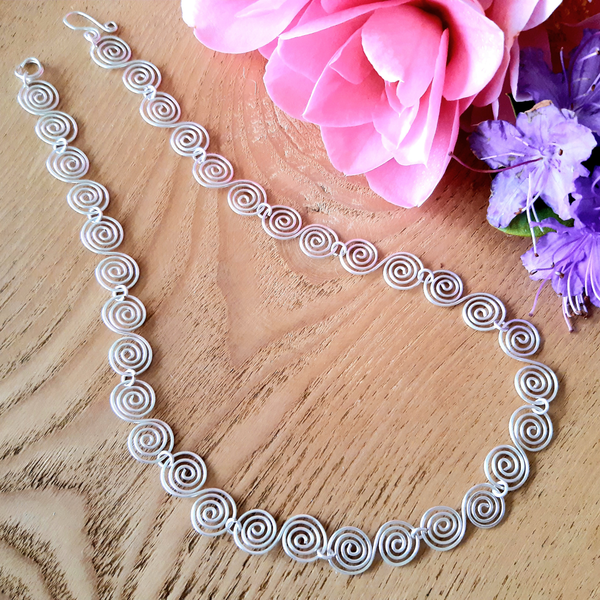 Silver spiral necklace on a wooden surface with pink and blue flowers