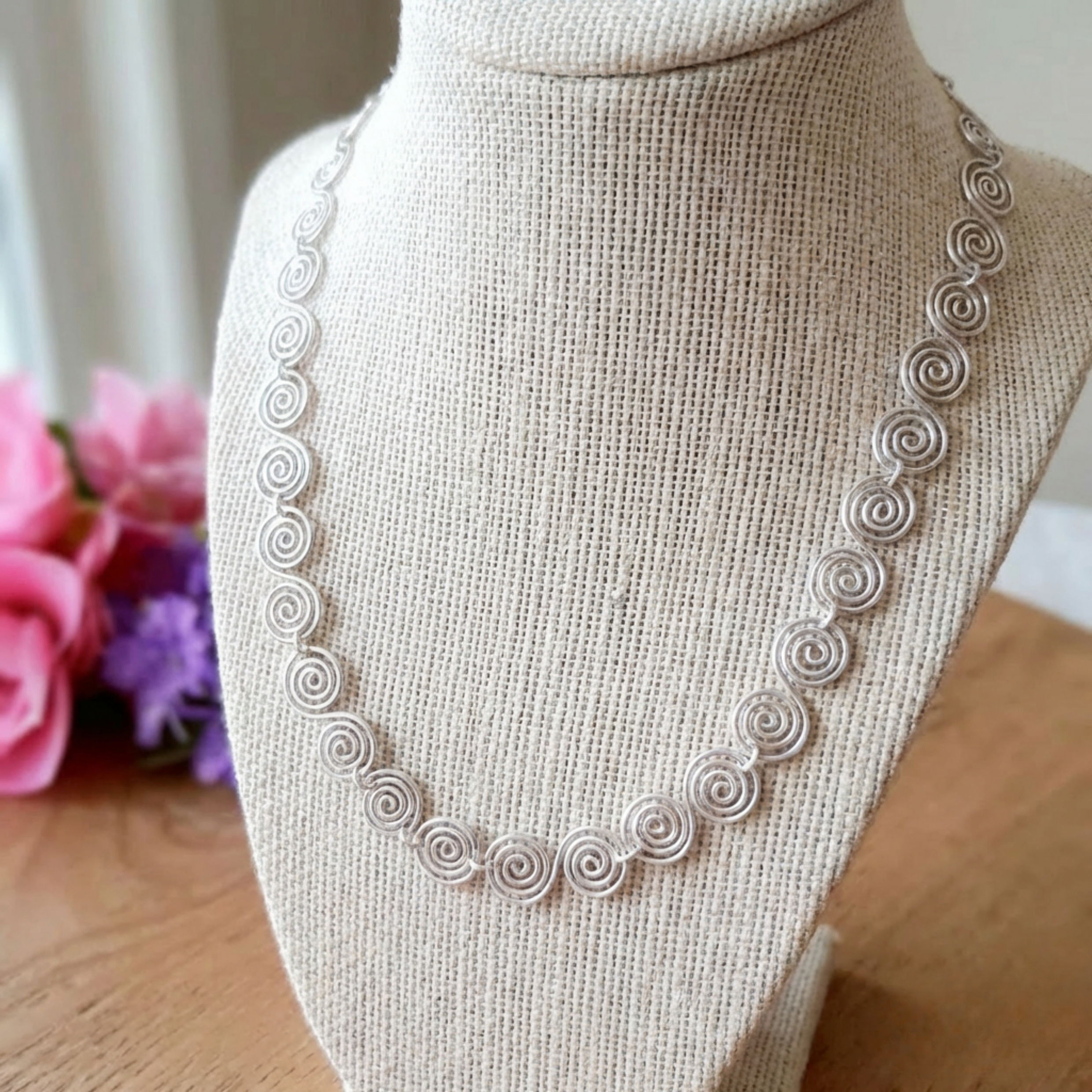Silver necklace on a mannequin bust with flowers in the background