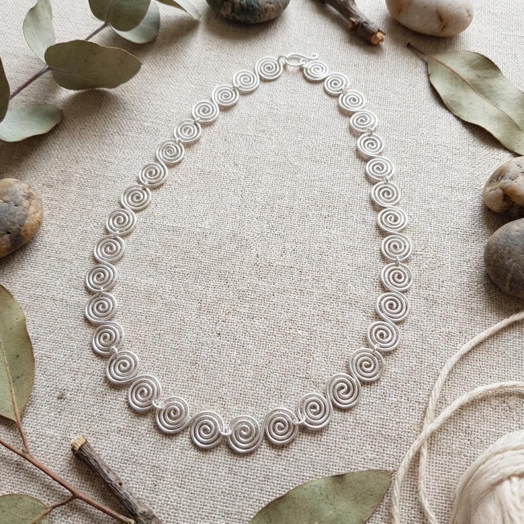 Delicate silver spiral necklace laying flat on fabric