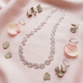 Silver spiral necklace on a pink satin background with petals