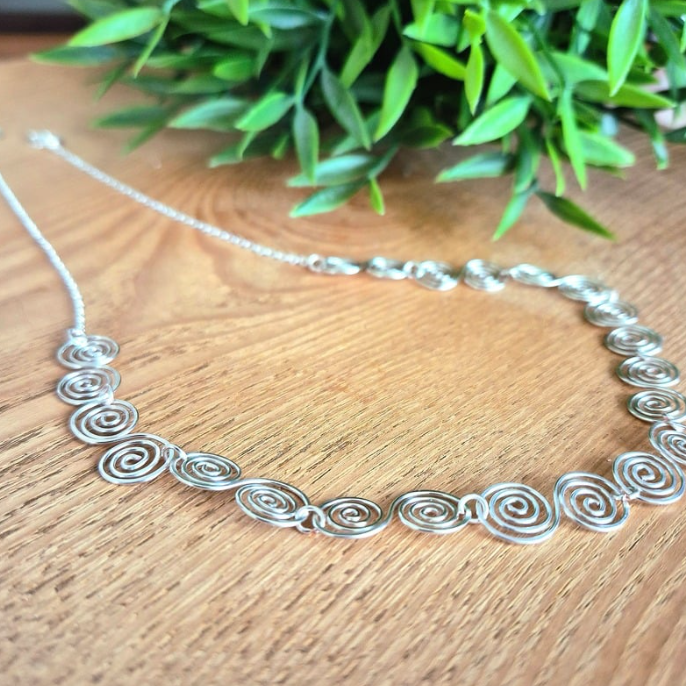 Half Chain half silver Celtic spirals necklace on a wooden surface