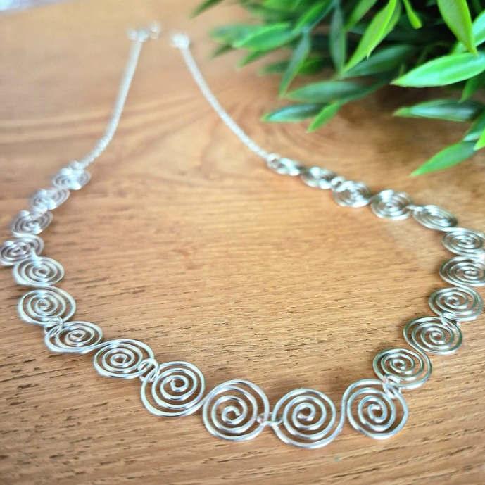 Detailed up close view of a Celtic silver spiral necklace with a chain on a wooden surface