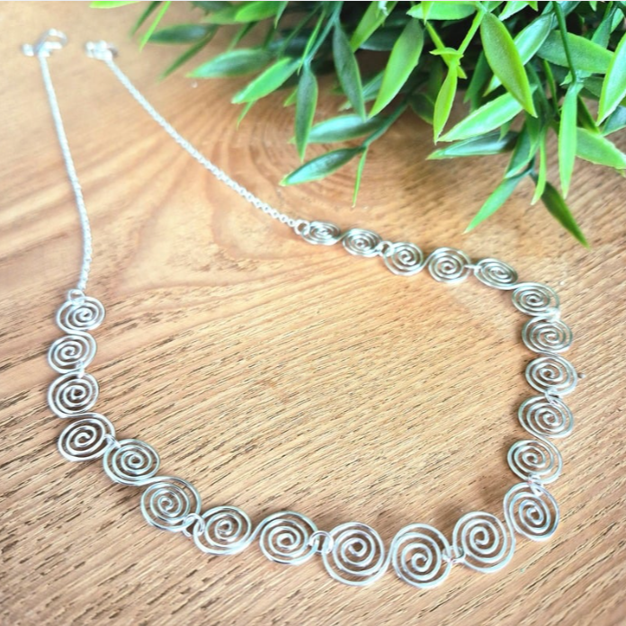 Celtic silver spiral necklace with half chain on a wooden surface