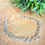 Celtic silver spiral necklace with half chain on a wooden surface