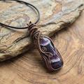 Amethyst pendant with copper wire wrapping on a wooden surface