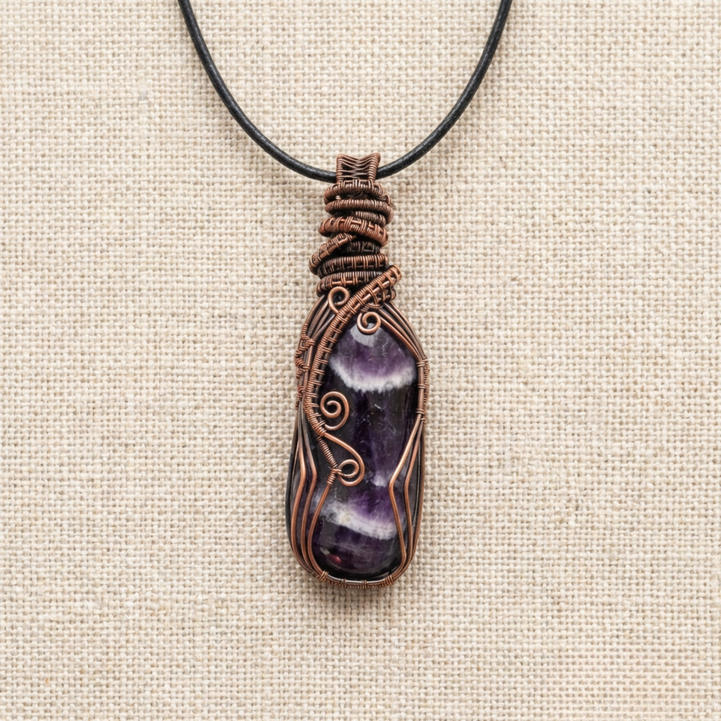 Purple stone pendant with copper wire wrapping on a beige fabric background