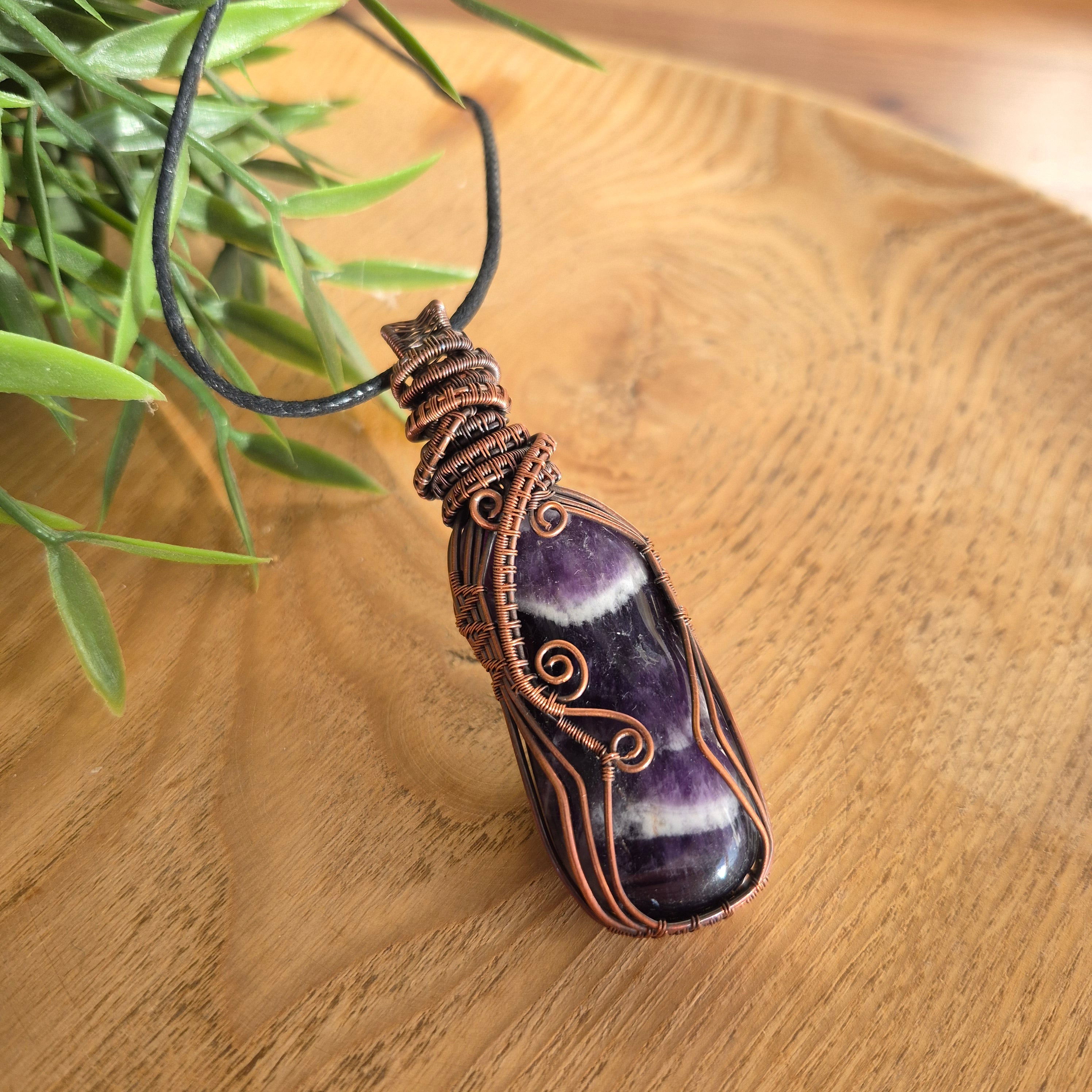 Amethyst pendant with copper wire wrapping on a wooden surface with a plant