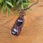 Amethyst crystal pendant with copper wire wrapping on a wooden surface with greenery.