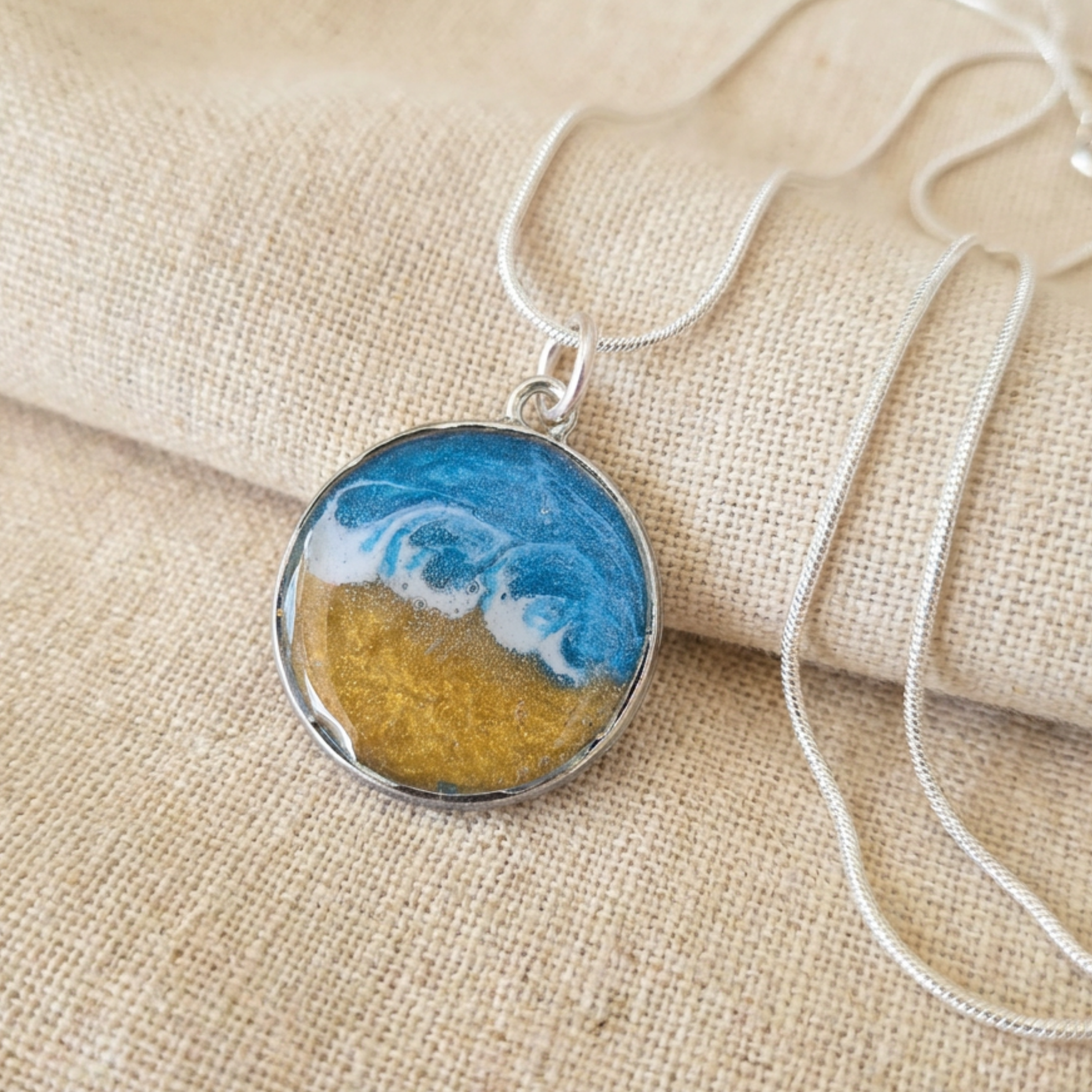 Silver pendant with a blue and gold centre with a wave effect on a fabric surface