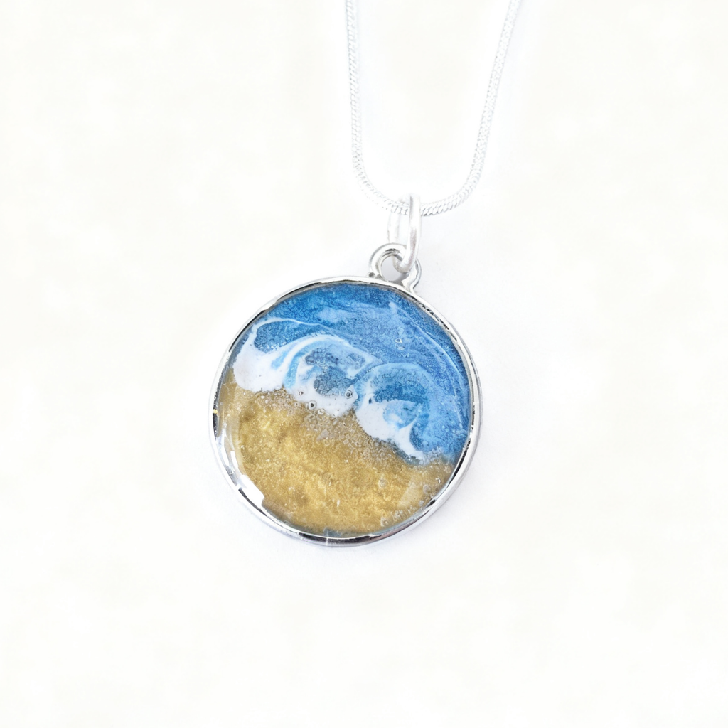 Necklace with a pendant featuring blue wave and gold sand design on a white background