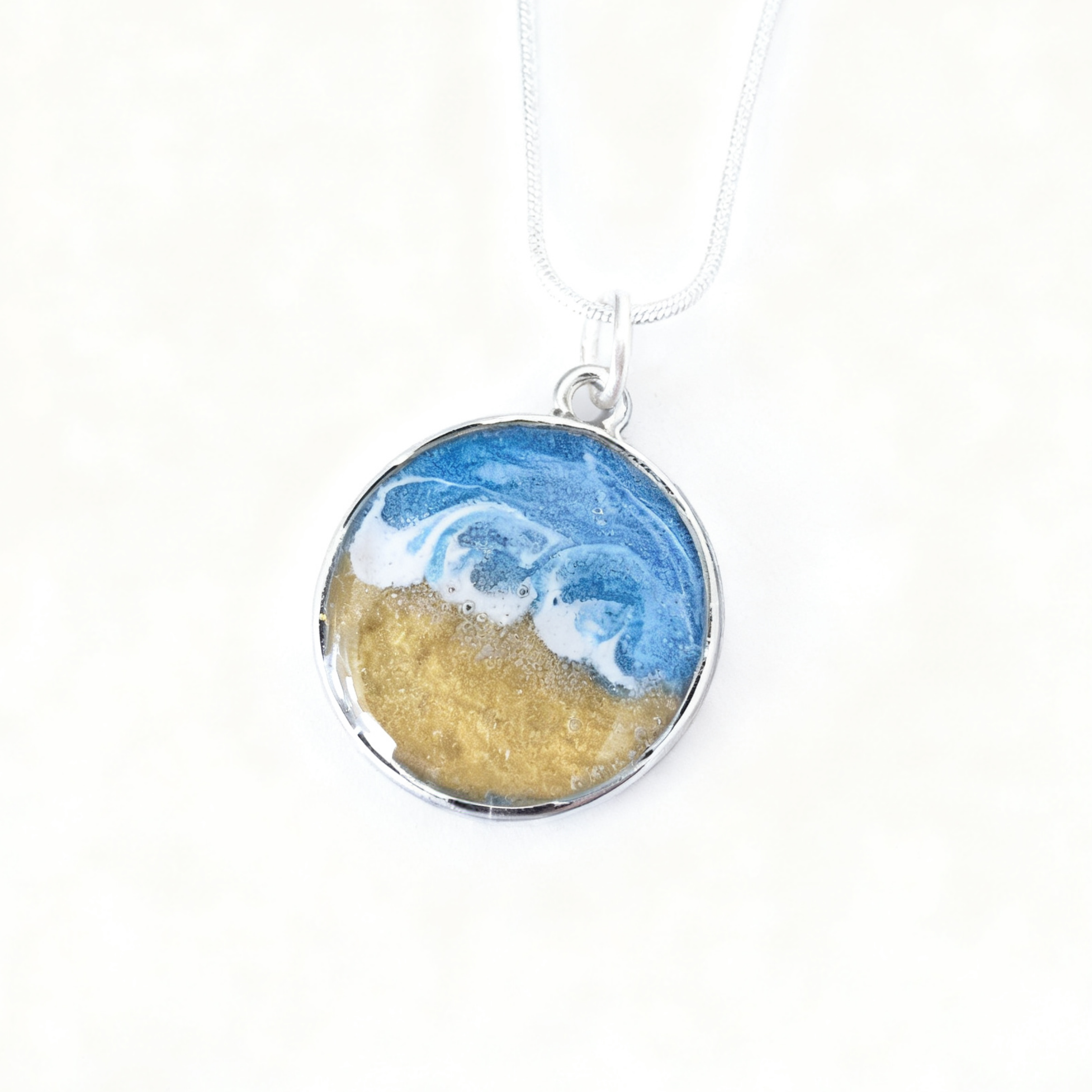 Necklace with a pendant featuring blue wave and gold sand design on a white background