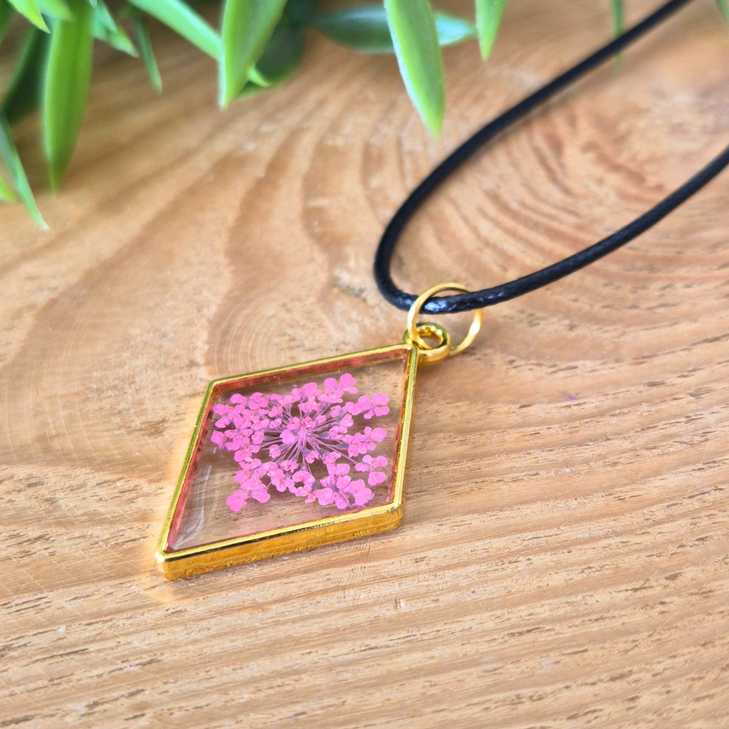Necklace with a diamond-shaped pendant featuring pink flowers on a wooden surface.