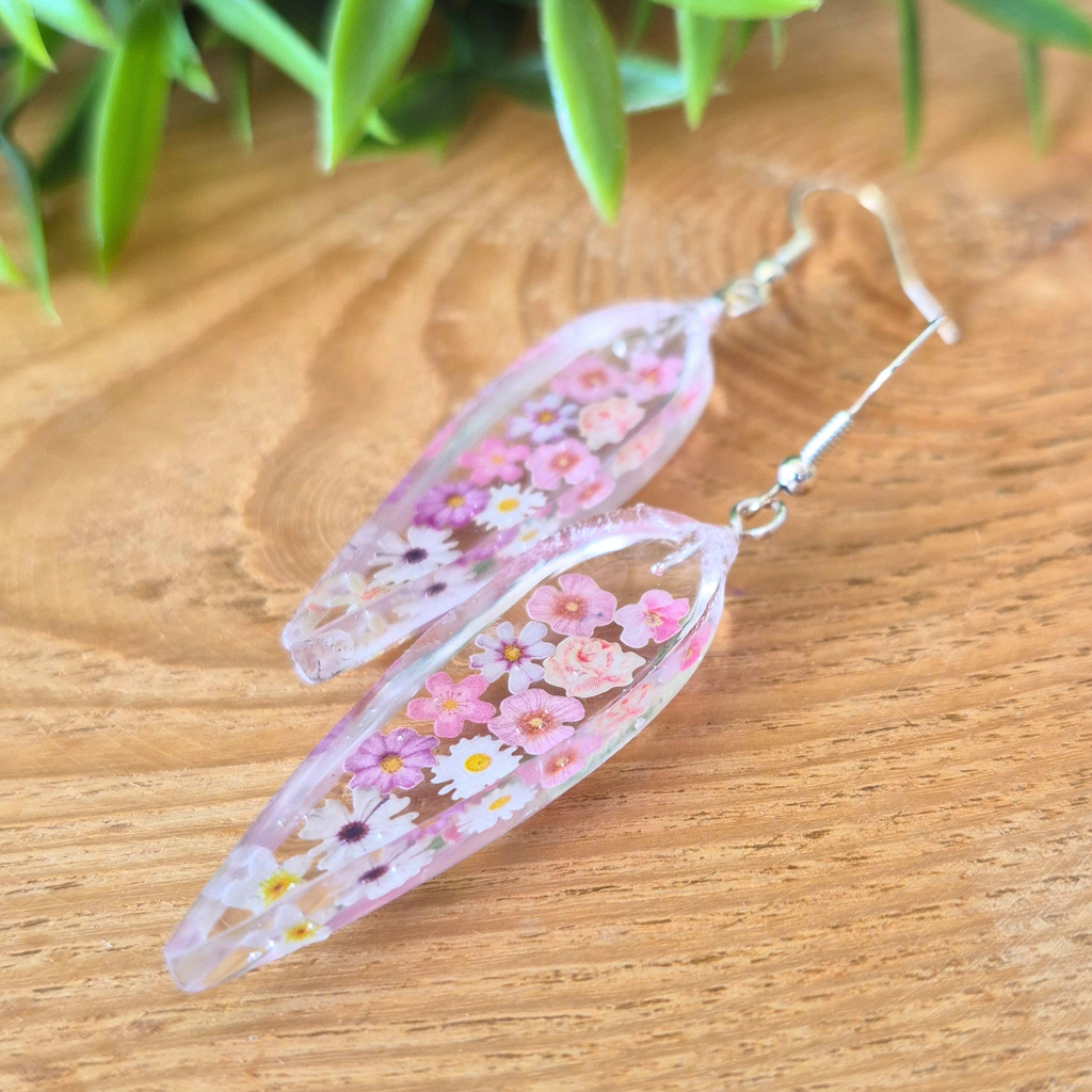 Floral earrings on a wooden surface with green leaves in the background
