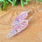 Floral earrings on a wooden surface with green leaves in the background