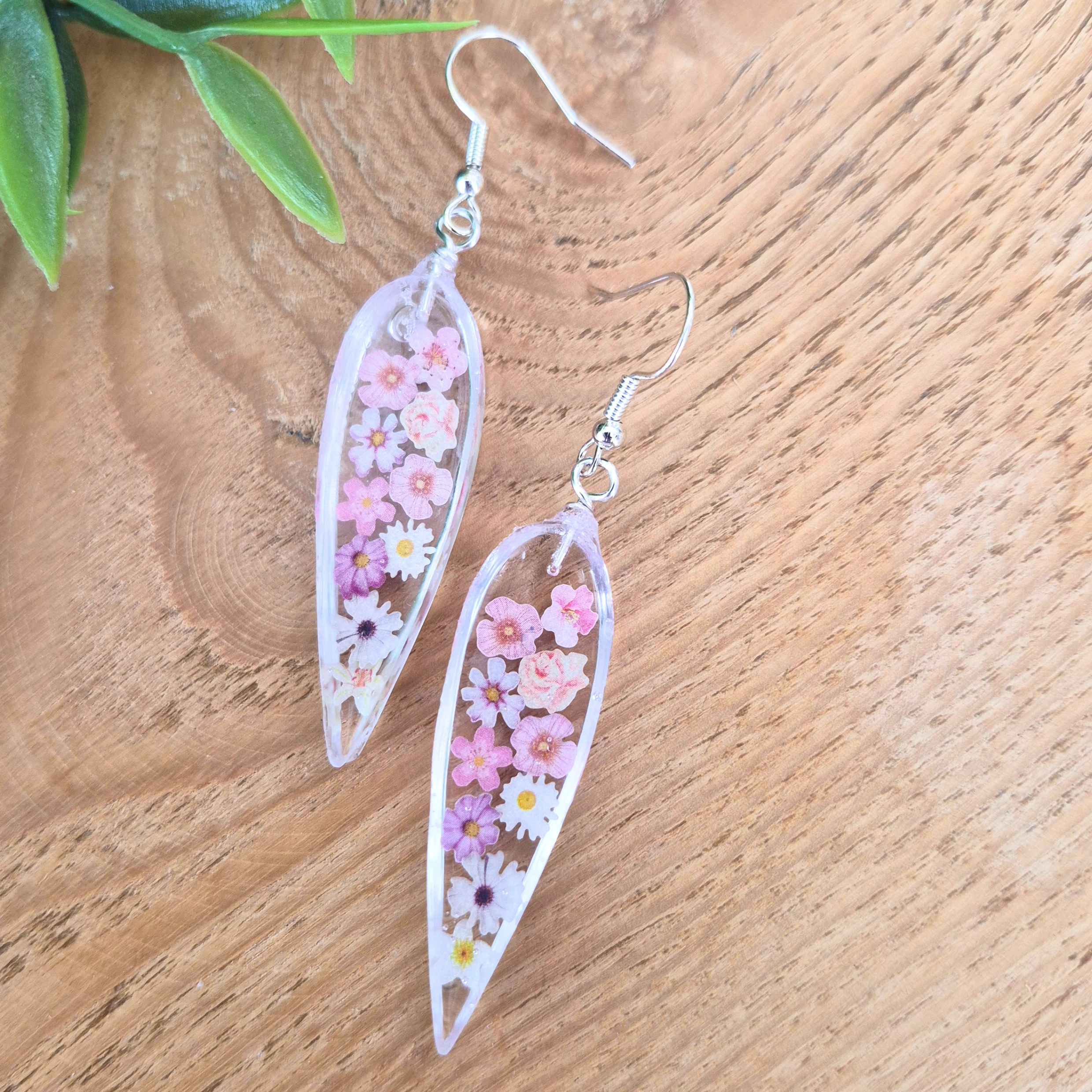 Teardrop-shaped floral earrings on a wooden surface with green leaves in the background