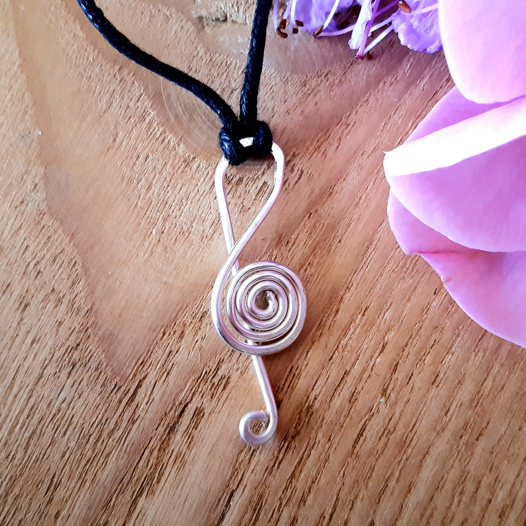 Wire music note pendant on a black cord with a pink flower in the background