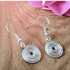 Silver spiral earrings on a wooden surface with pink flowers in the background