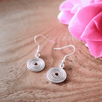 Silver spiral earrings on a wooden surface with pink flowers in the background