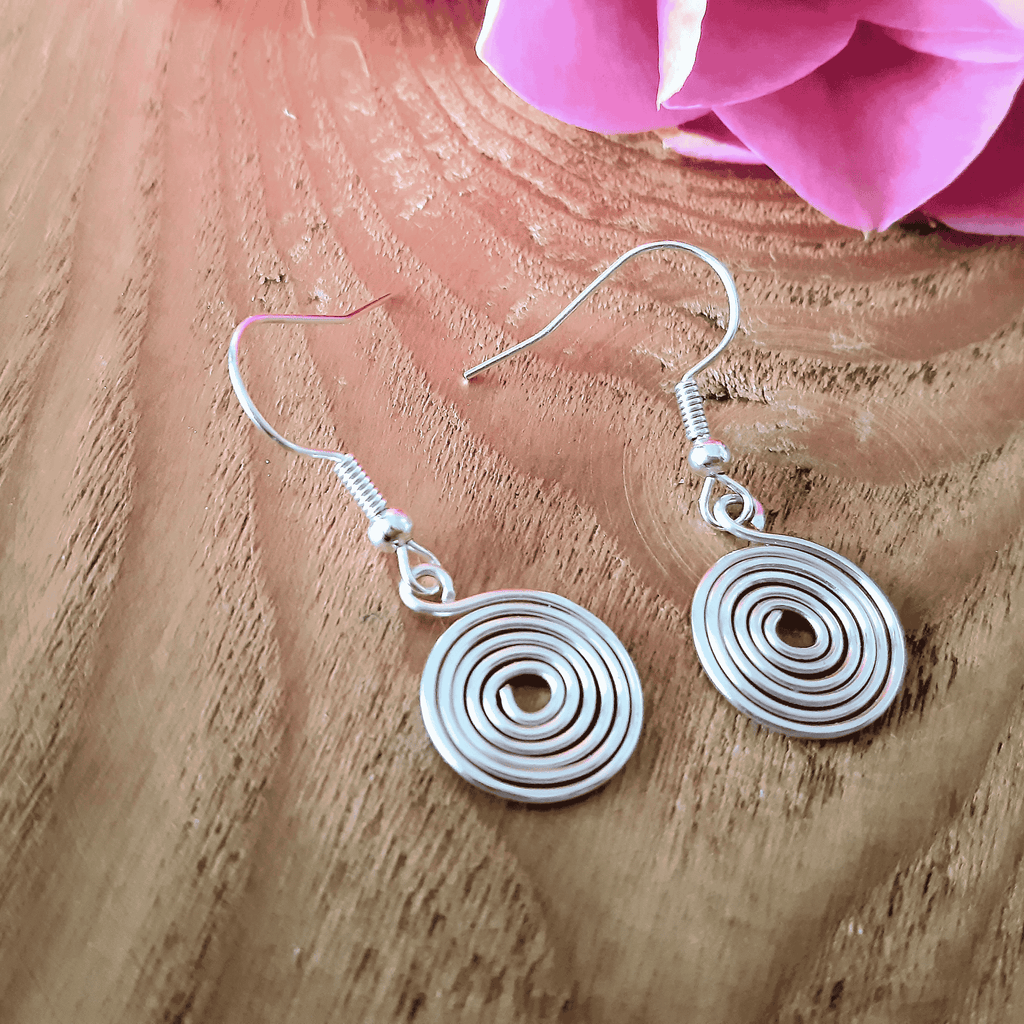 Silver spiral earrings on a wooden surface with pink flowers in the background