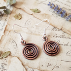 Closed copper spiral earrings on light wood background, handmade copper jewellery UK
