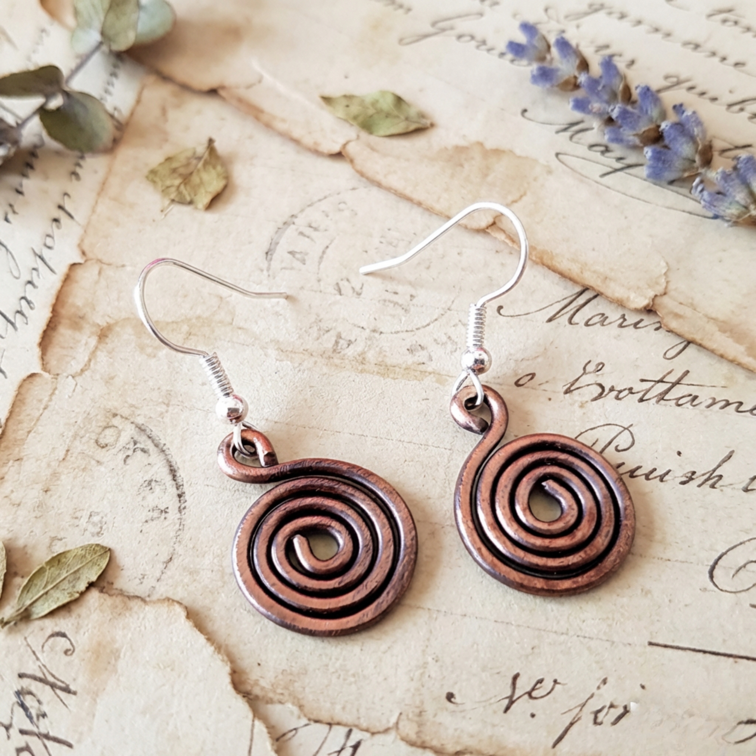 Closed copper spiral earrings on light wood background, handmade copper jewellery UK