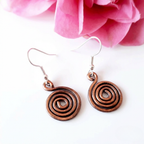 Copper spiral earrings on a white background with pink flowers.