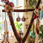 Decorative wooden frame with flowers, feathers, and spiral earrings in a bohemian-style room.