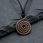 Bronzed copper spiral pendant on a black cord against a dark stone background