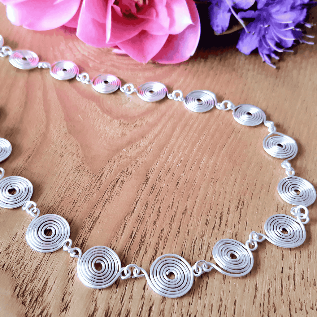 Detailed view of a closed silver spiral necklace on a wooden background with flowers