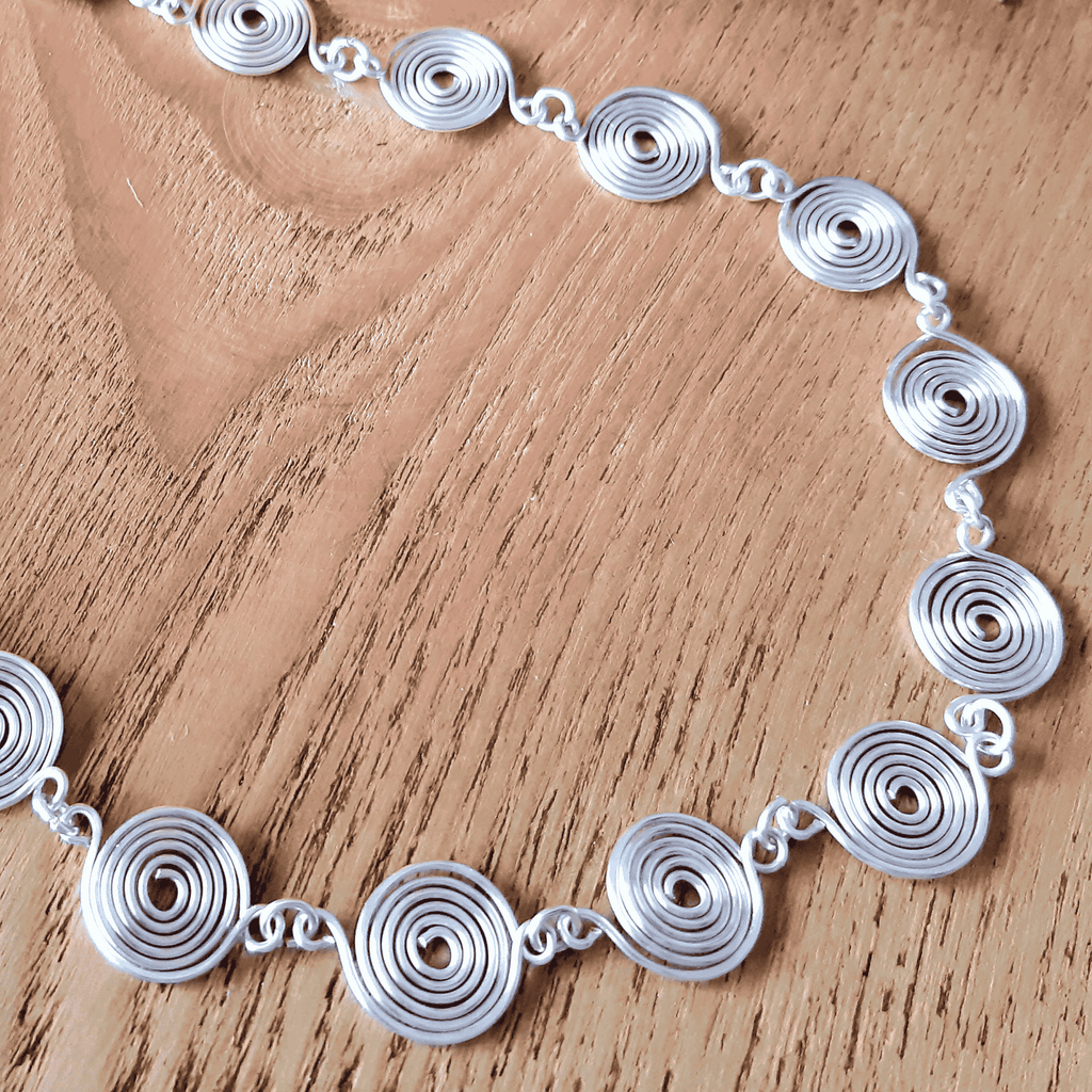 Close up view of the disc like spirals on a closed silver spiral necklace on a wooden background