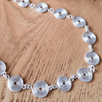 Close up view of the disc like spirals on a closed silver spiral necklace on a wooden background