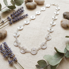 Silver necklace with circular design on a textured surface with lavender and eucalyptus leaves.