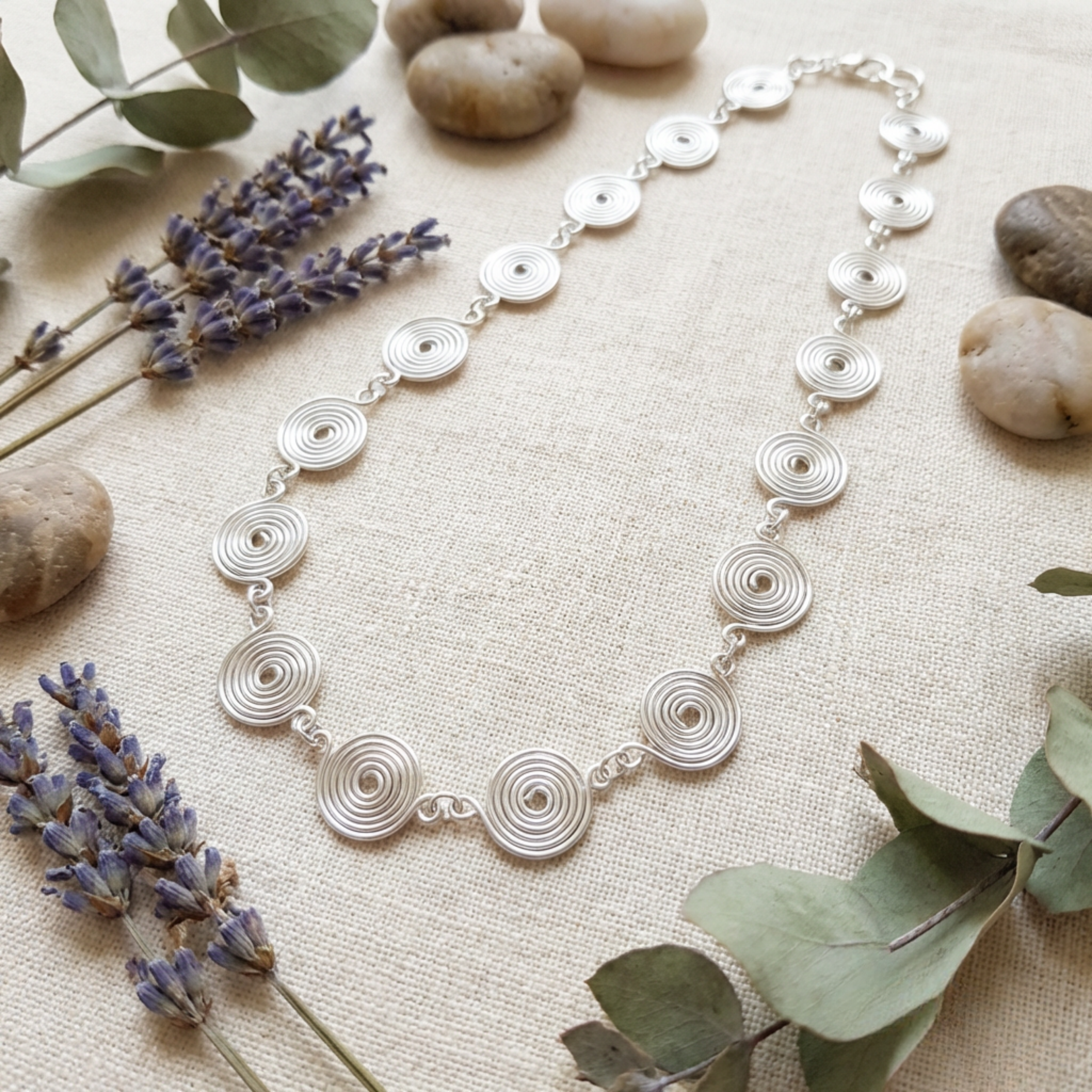 Silver necklace with circular design on a textured surface with lavender and eucalyptus leaves.