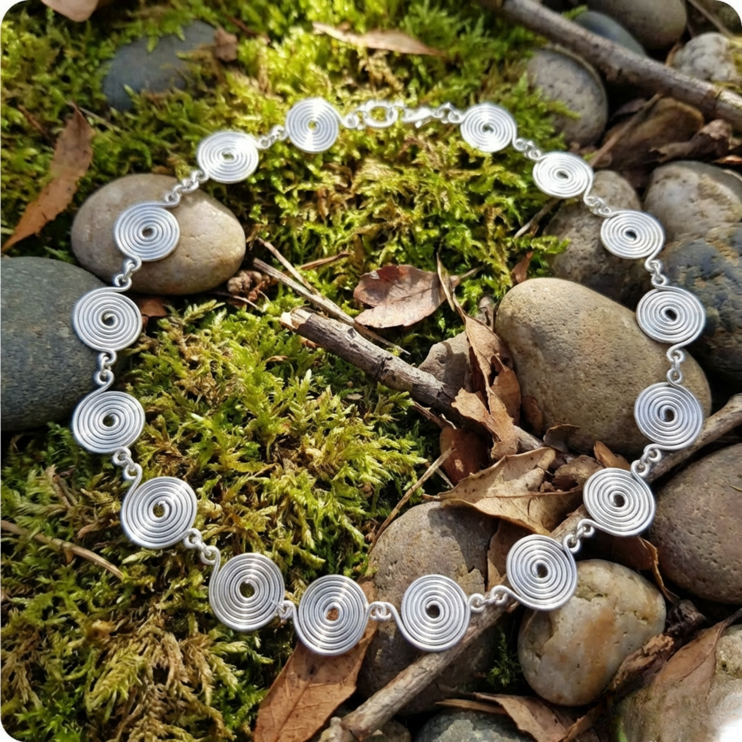 Silver spiral necklace with circular patterns on a natural background of moss and stones