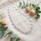 Silver necklace with circular patterns on a light background with flowers and greenery.