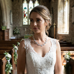 Woman in a white wedding dress standing in a church with stained glass windows. Wearing a silver spiral statement necklace