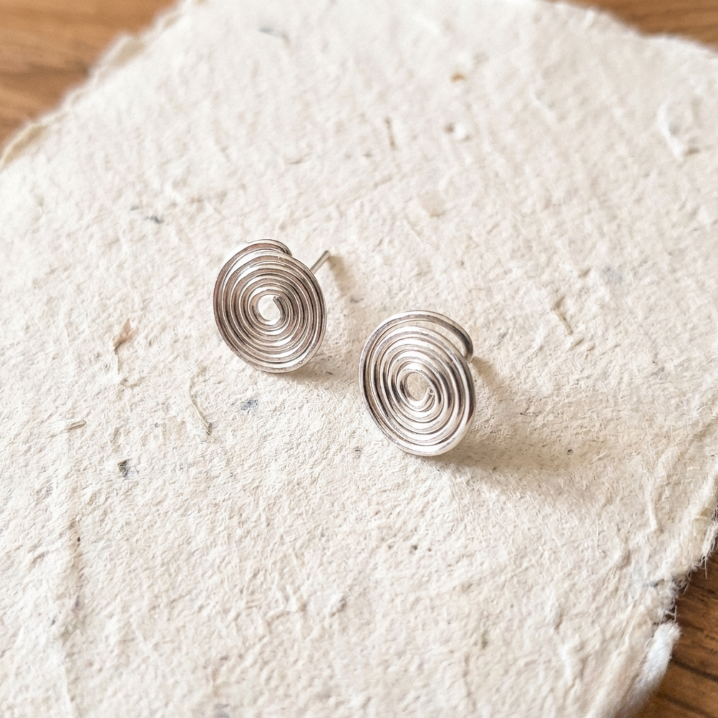 Silver spiral earrings on a textured white surface