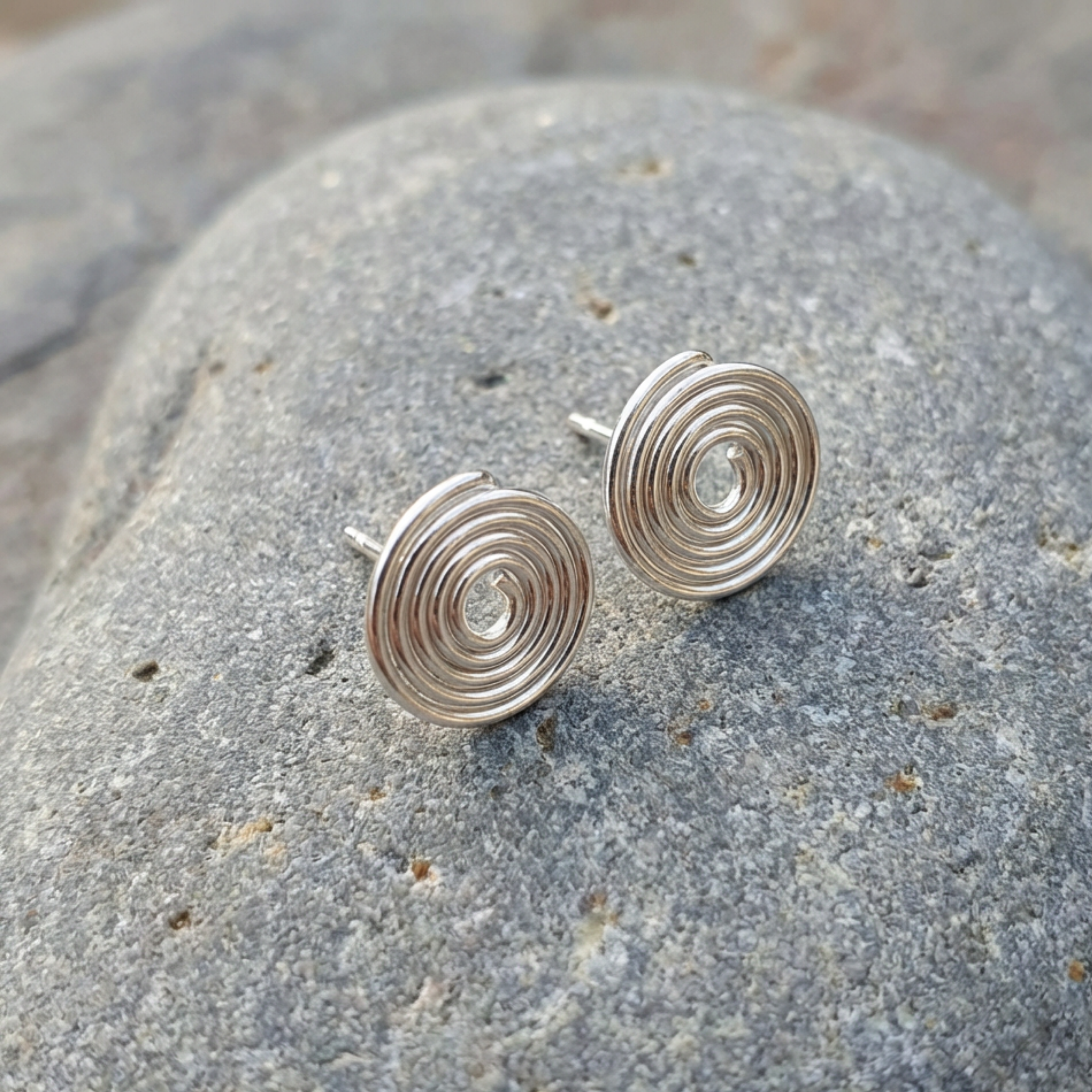 Silver spiral earrings on a stone surface